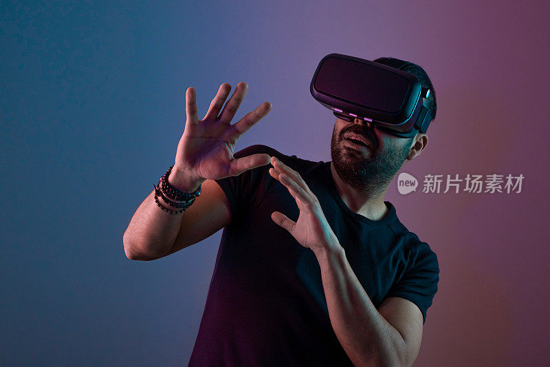 戴着VR眼镜的年轻人兴奋地与虚拟现实在彩色霓虹灯、未来科技、教育视频游戏中互动