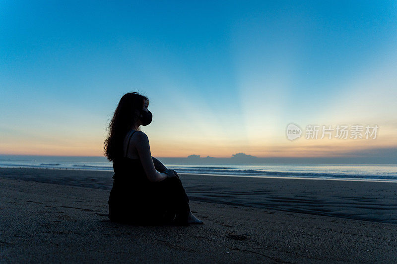 年轻的亚洲女子站在海边看日出