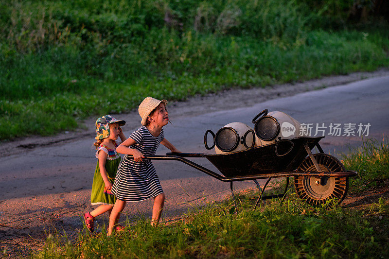在一个公共有机花园里，一个小女孩用手推车搬运木桶，去收集河水灌溉他们的田地