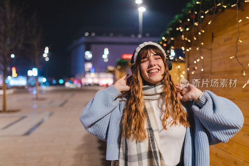 微笑的年轻女子在城市的夜晚听音乐