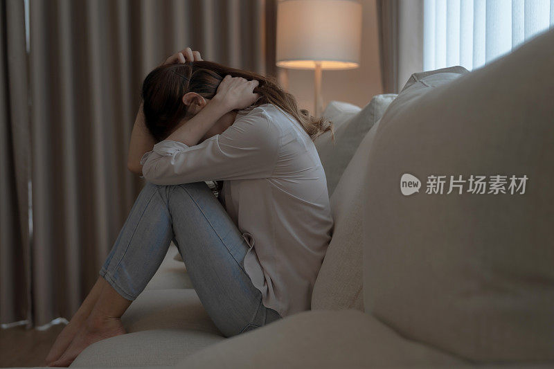 亚洲女性独自坐在客厅感到沮丧和压力。
