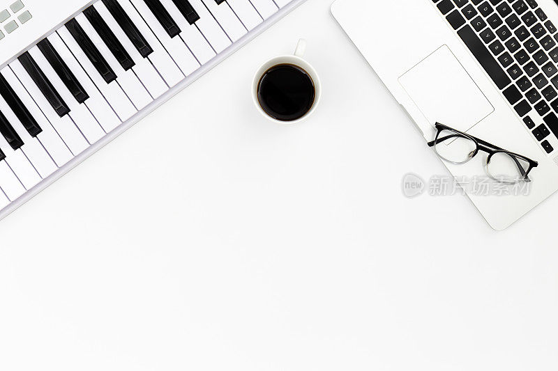 钢琴、笔记本电脑、眼镜和一杯咖啡放在白色的背景上，平躺着。