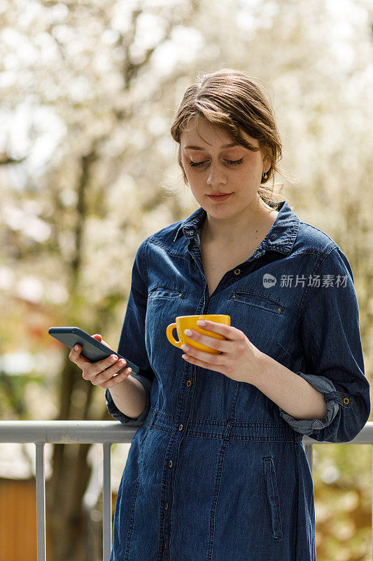 年轻女子站在阳台上，一边喝咖啡一边打电话