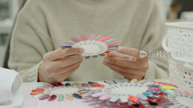 年轻的亚洲女性顾客在美甲美容院挑选指甲油色板，修指甲