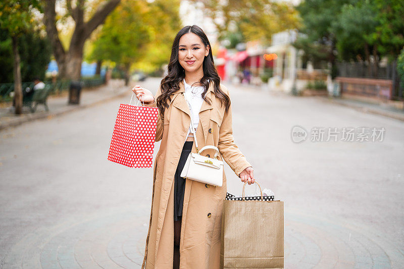 年轻的亚洲女人在街上拎着购物袋。购物的概念