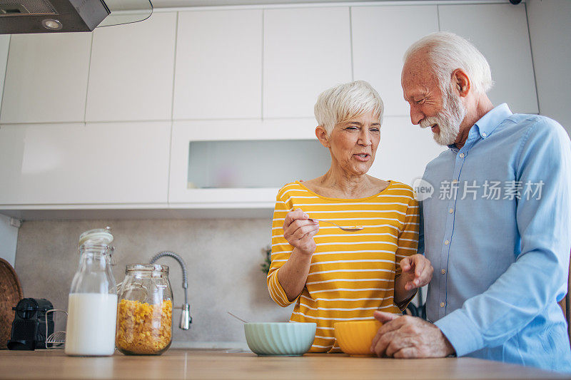 一对年长的异性恋夫妇在厨房里享受时光。一对年长的异性恋夫妇在厨房里享受时光。女人拿着勺子。