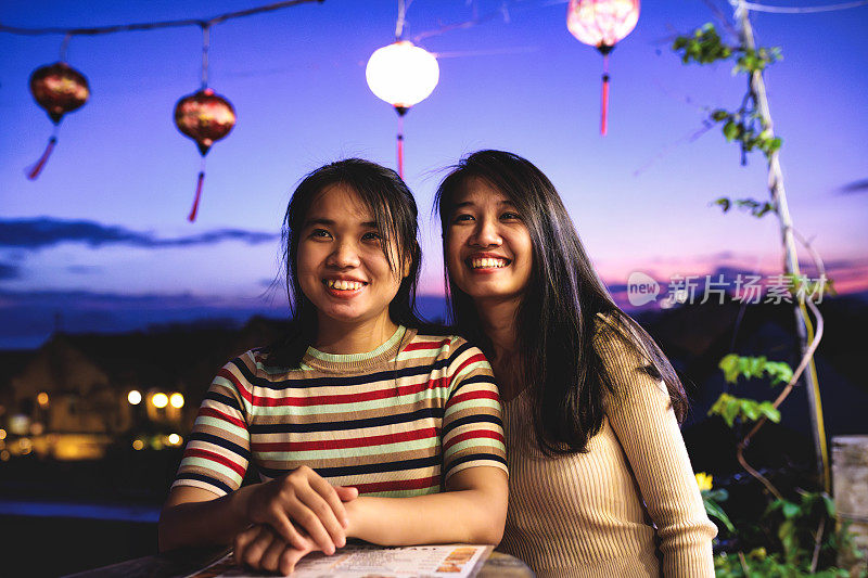 两个快乐的年轻亚洲女人晚上在会安老城的屋顶酒吧