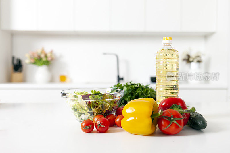 白色现代厨房的桌子上放着沙拉的配料，蔬菜、西红柿、辣椒和一瓶油