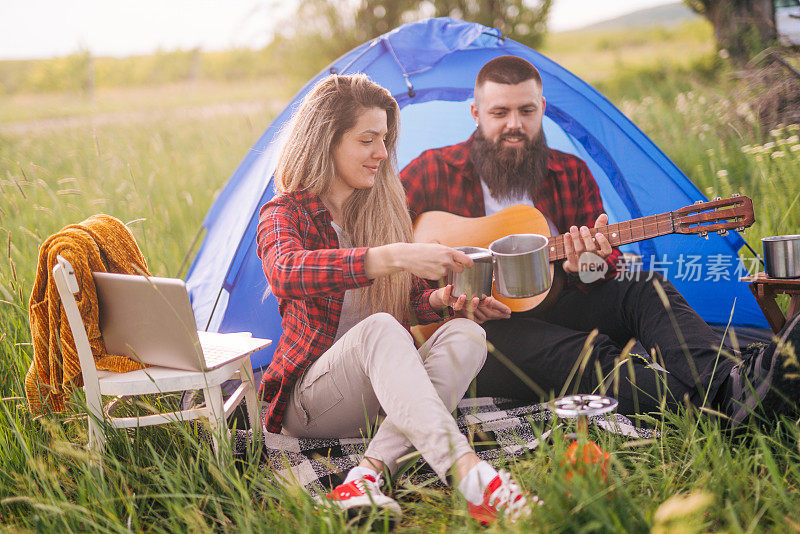 一对年轻夫妇在大自然中露营，一个男人在弹吉他，他们在一起玩得很开心