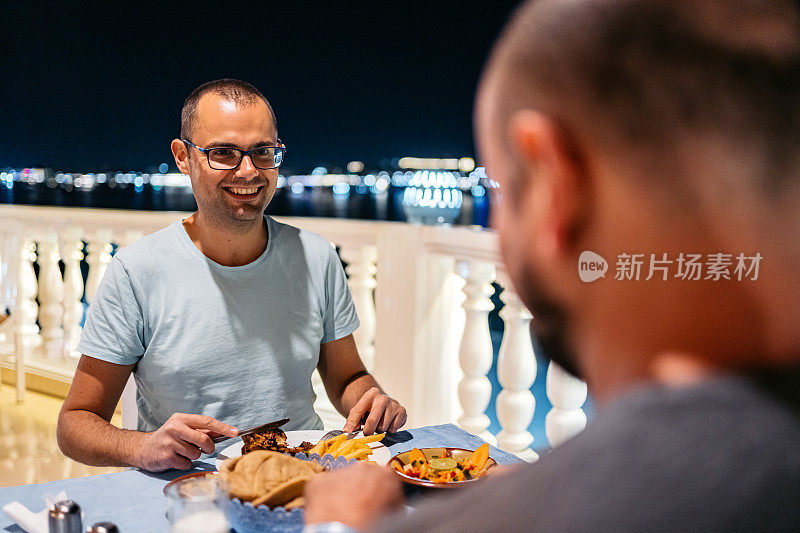 在埃及卢克索，两个朋友在俯瞰尼罗河夜景的餐厅阳台上共进晚餐