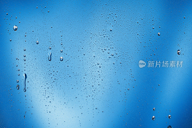 凝结或雨滴落在玻璃上。冰冷的磨砂玻璃，蓝色背景上有水滴