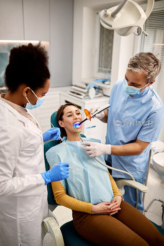 牙科助理在女病人牙科手术中使用紫外线灯。