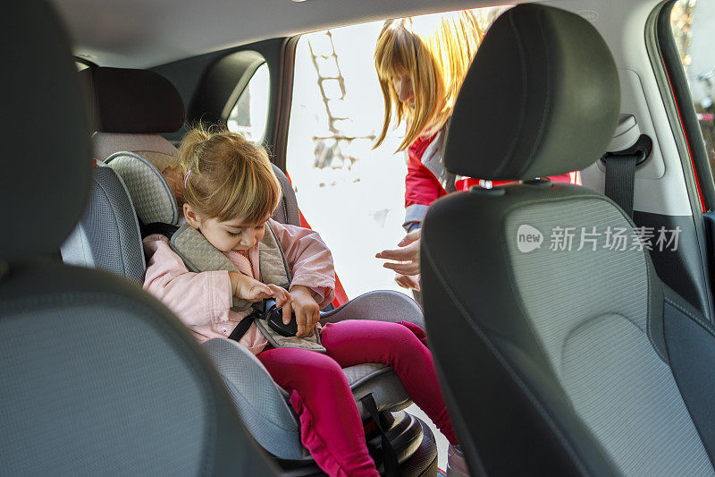 一位妇女在车上观察小孩玩安全带