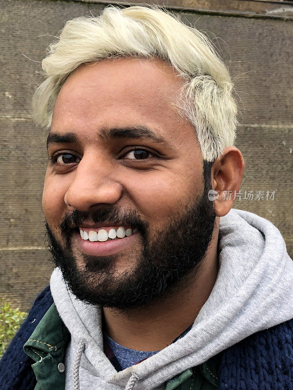 一名印度男子展示自己的新发型，黑色的头发被化学物质染成了金色，他微笑着看着相机，拍了头照
