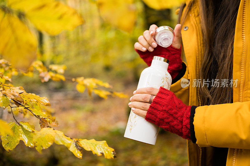 在森林里，一个女人打开了装着茶的白色保温瓶。