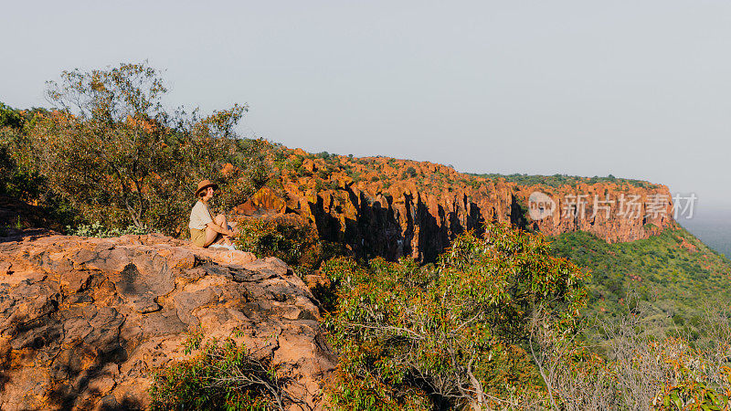 在纳米比亚的山顶上，一名女性旅行者凝视着落日的美景