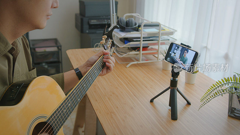 音乐家吉他手与钢琴家在家中通过视频通话进行原声吉他演奏。两名男子正在智能手机上通过远程办公技术进行音乐直播。