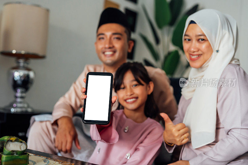 快乐的亚洲马来人女孩显示白色的空白屏幕在智能手机上与她的父母在家里