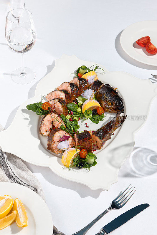 宴会菜肴——白色餐桌上的烟熏虹鳟鱼。优雅的熏鱼鳟鱼晚宴，婚礼，节日派对。宴会菜单的食物造型。