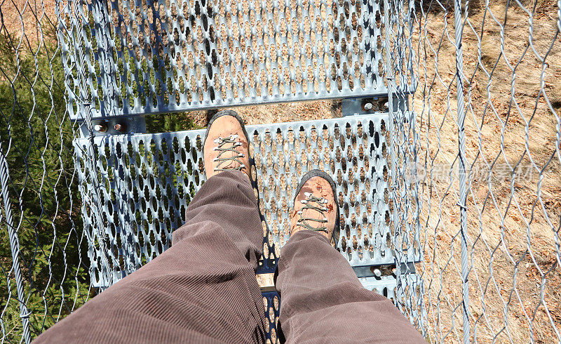 登山靴探险者在高空徒步行走在悬索桥上，没有眩晕症状