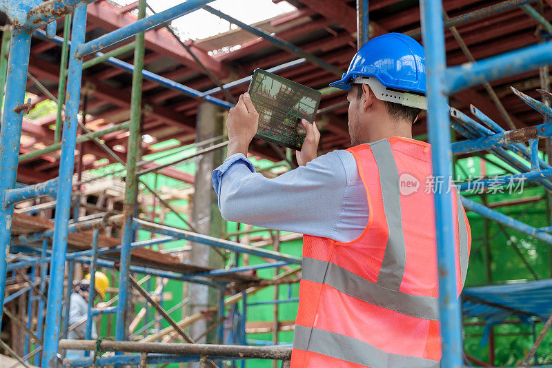 年轻的亚洲建筑工人在建筑工地使用平板电脑。