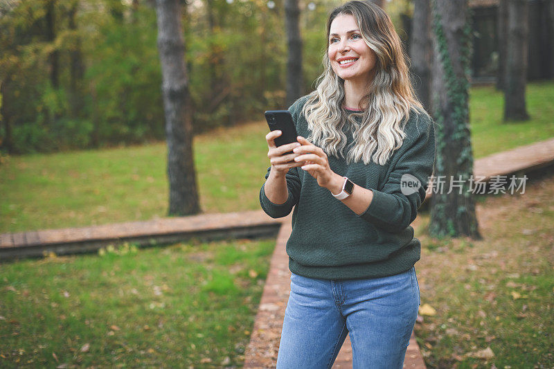 美丽的女人走在她的小屋花园拿着手机