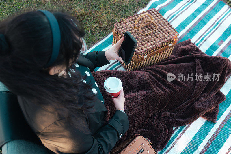 智能手机上的拉丁女子-野餐和一杯咖啡-专注于手机