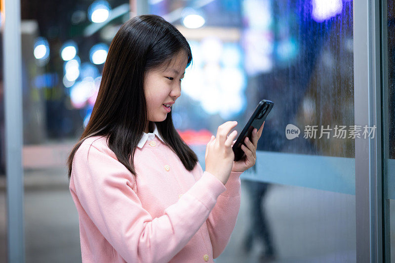 亚洲女孩晚上在城市街道上使用智能手机