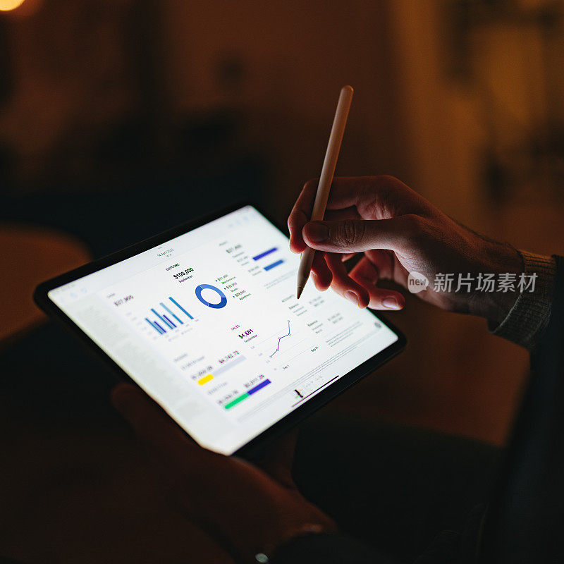 一名男子晚上在家办公室用笔在数字平板电脑上写商业报告的特写照片
