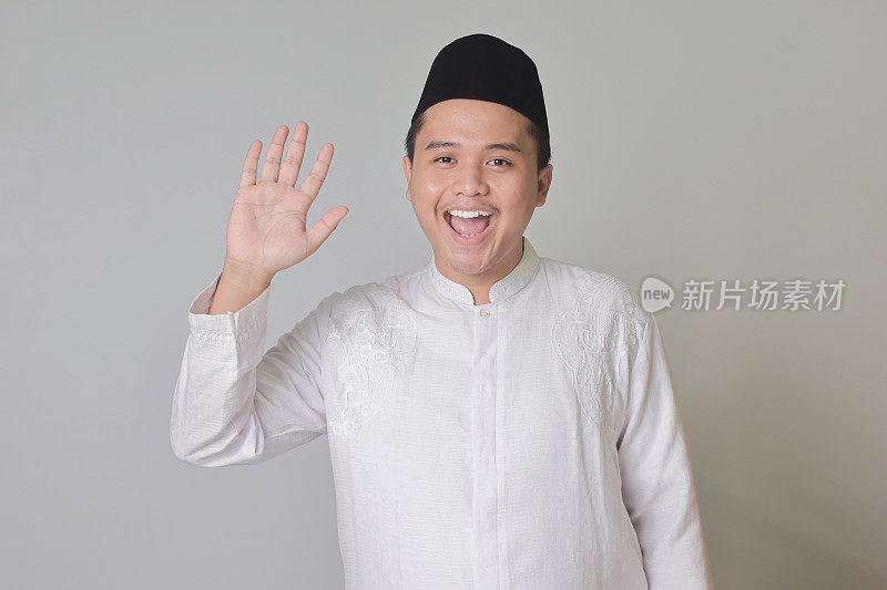 亚洲穆斯林男子说嗨，对着镜头挥手，用幸福的微笑问候人
