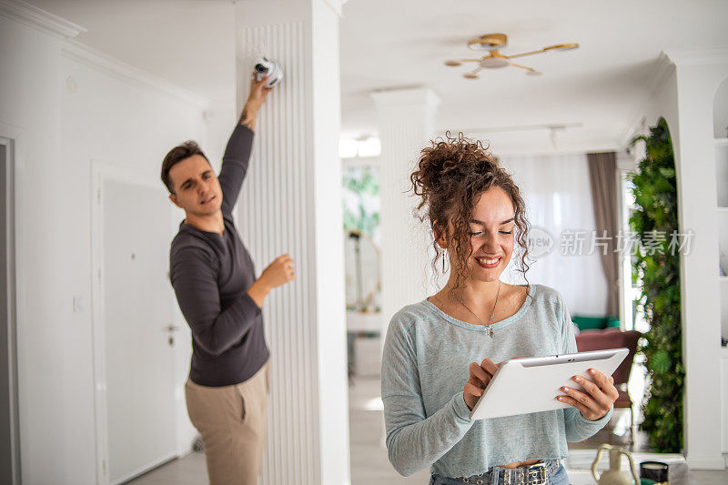 一对年轻夫妇，一男一女，正在他们的公寓里安装家庭监控摄像头