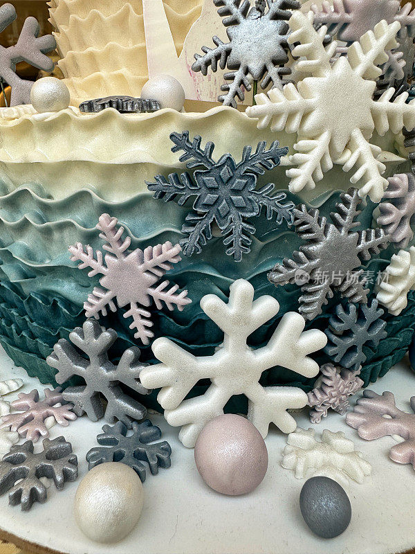 冬季主题分层生日蛋糕表面的全帧图像装饰在蛋糕板上，彩色黄油糖衣，珠光翻糖糖衣形状像球和雪花，重点在前景
