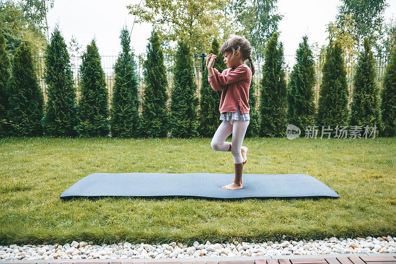 可爱的小女孩，5-6岁，在户外练习瑜伽时站在鹰式或鹰式