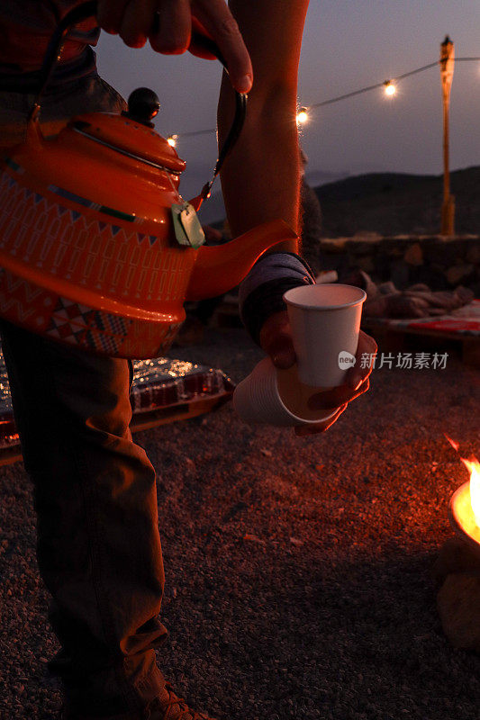 在寒冷的秋夜，在山间营地用篝火从水壶里倒茶