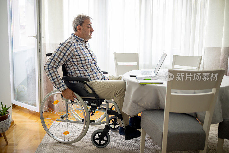 中年残疾高加索人坐在轮椅上，在家工作时用笔记本电脑进行视频通话