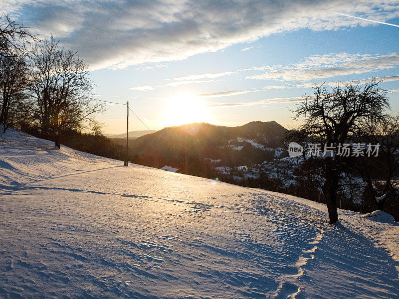 日落时的冬日风景，白雪覆盖的山丘和晴朗的天空。