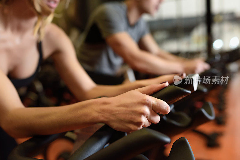 两人在健身房骑自行车，锻炼双腿做有氧运动骑自行车。