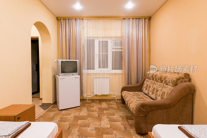 一个小房间的内部有沙发床和两张单人床，窗户，电视和冰箱