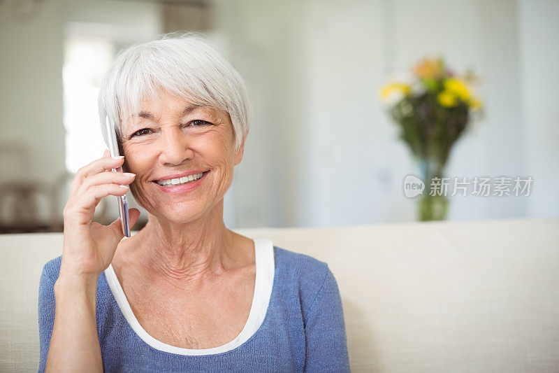 微笑的年长妇女在客厅里用手机聊天