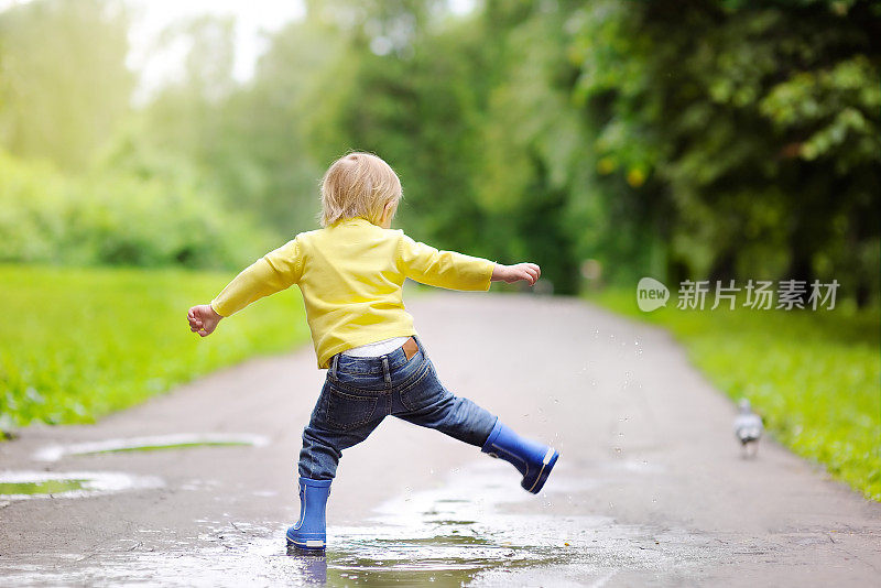 小男孩穿着雨靴在水池里跳