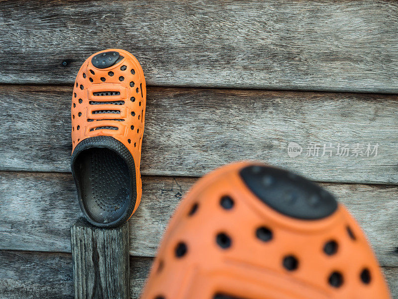 一双橙色的橡胶拖鞋在旧木头上