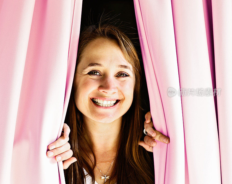 欢迎光临!金发美女透过粉红色的窗帘，开心地微笑着