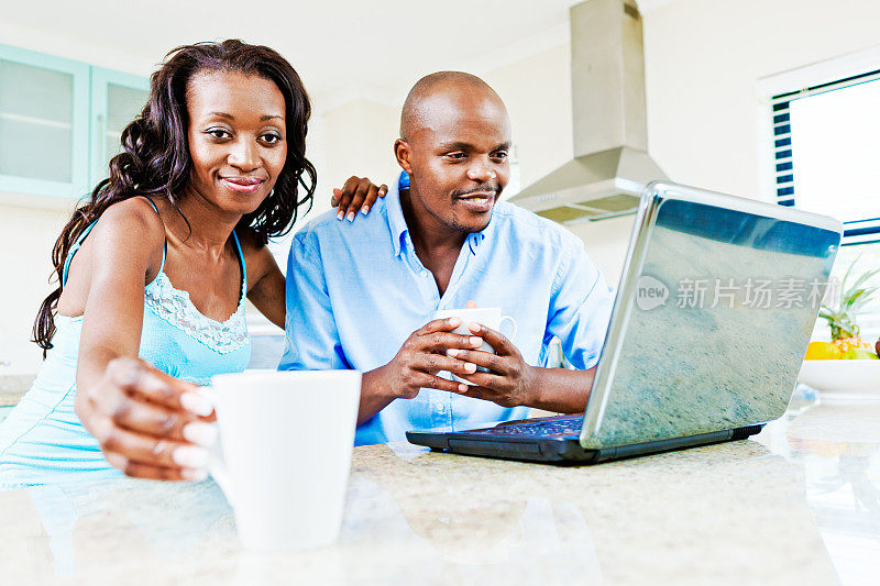 一对幸福的年轻夫妇在厨房柜台上拿着笔记本电脑和咖啡