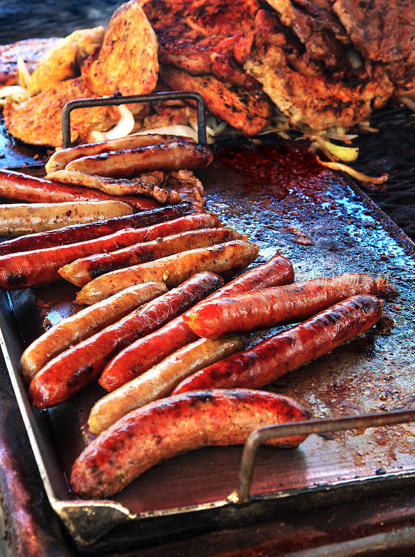 在食品摊贩的烤架上烤着的德式香肠和猪排