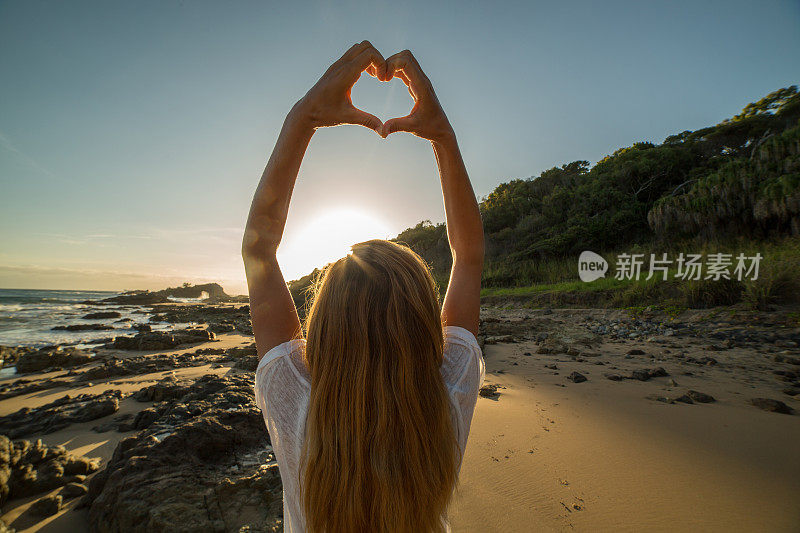 年轻女子把海滩上的夕阳画成心形