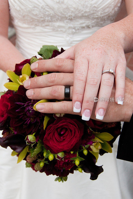白种人新娘和新郎的手在彩色婚礼花束上休息