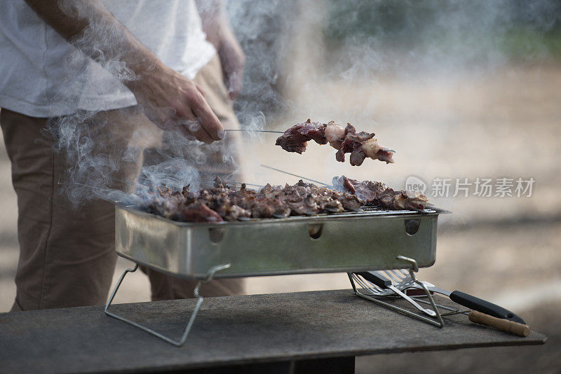 在一个便携式木炭烤架上准备牛肉的人。