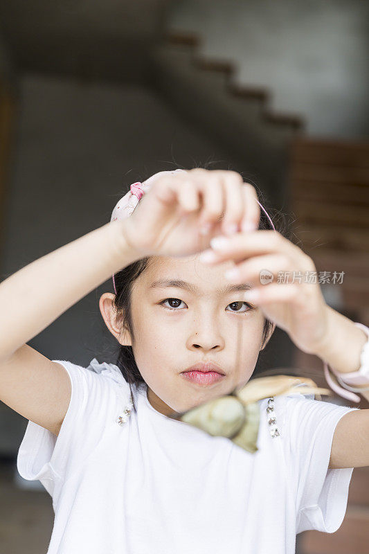 小女孩用一根棕叶绳提着粽子。