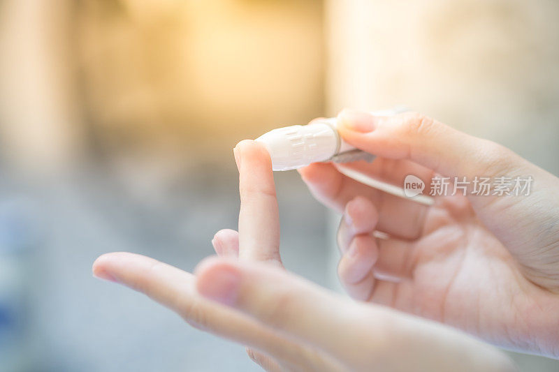 近距离亚洲妇女的手使用柳叶刀的手指检查血糖水平的血糖仪