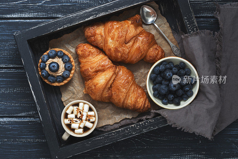 羊角面包，带蓝莓的蛋糕，木质托盘上放着棉花糖的咖啡和餐巾。